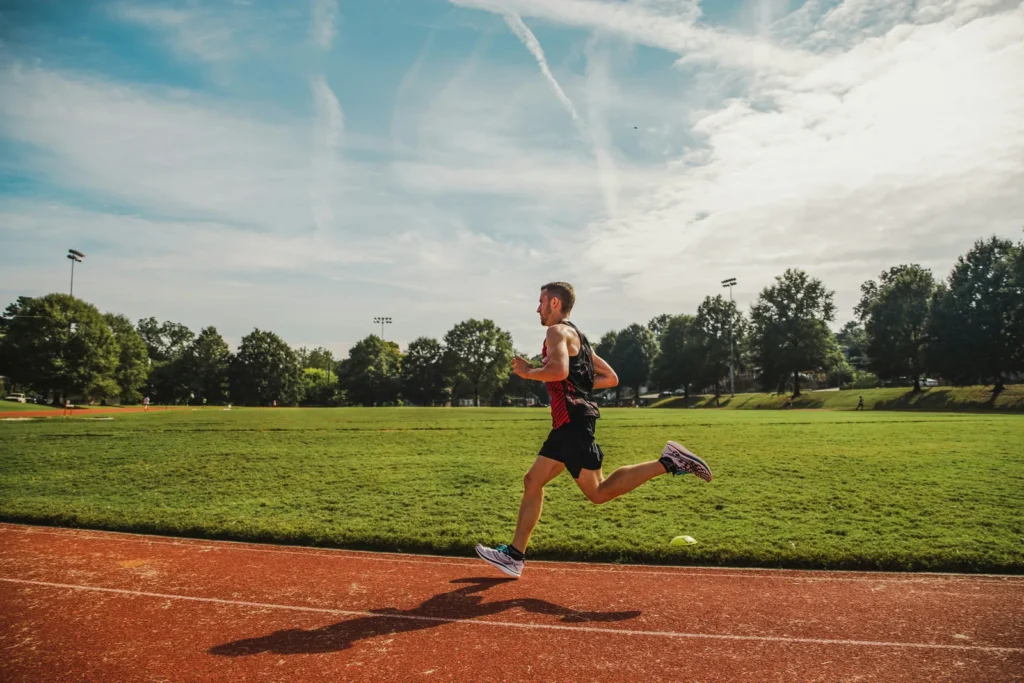 Coureur en pleine foulée sur une piste d'athlétisme, au bord d'un terrain en herbe